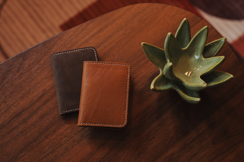 Two leather wallets on a wooden surface with a ceramic leaf-shaped object.