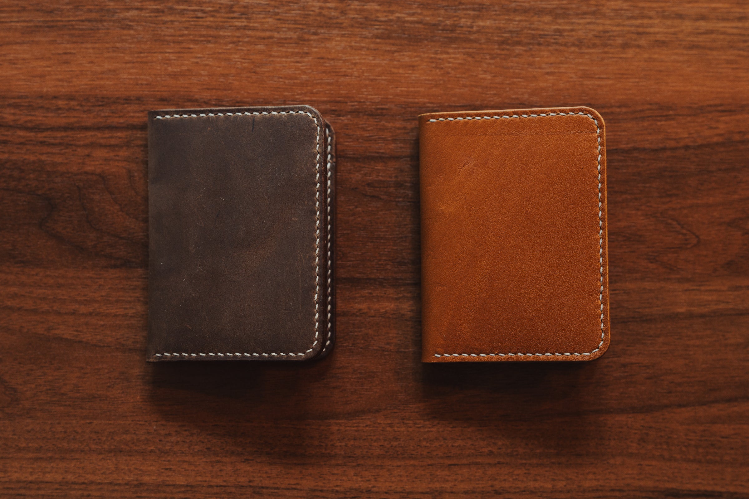 Two leather wallets, one brown and one black, on a wooden surface.