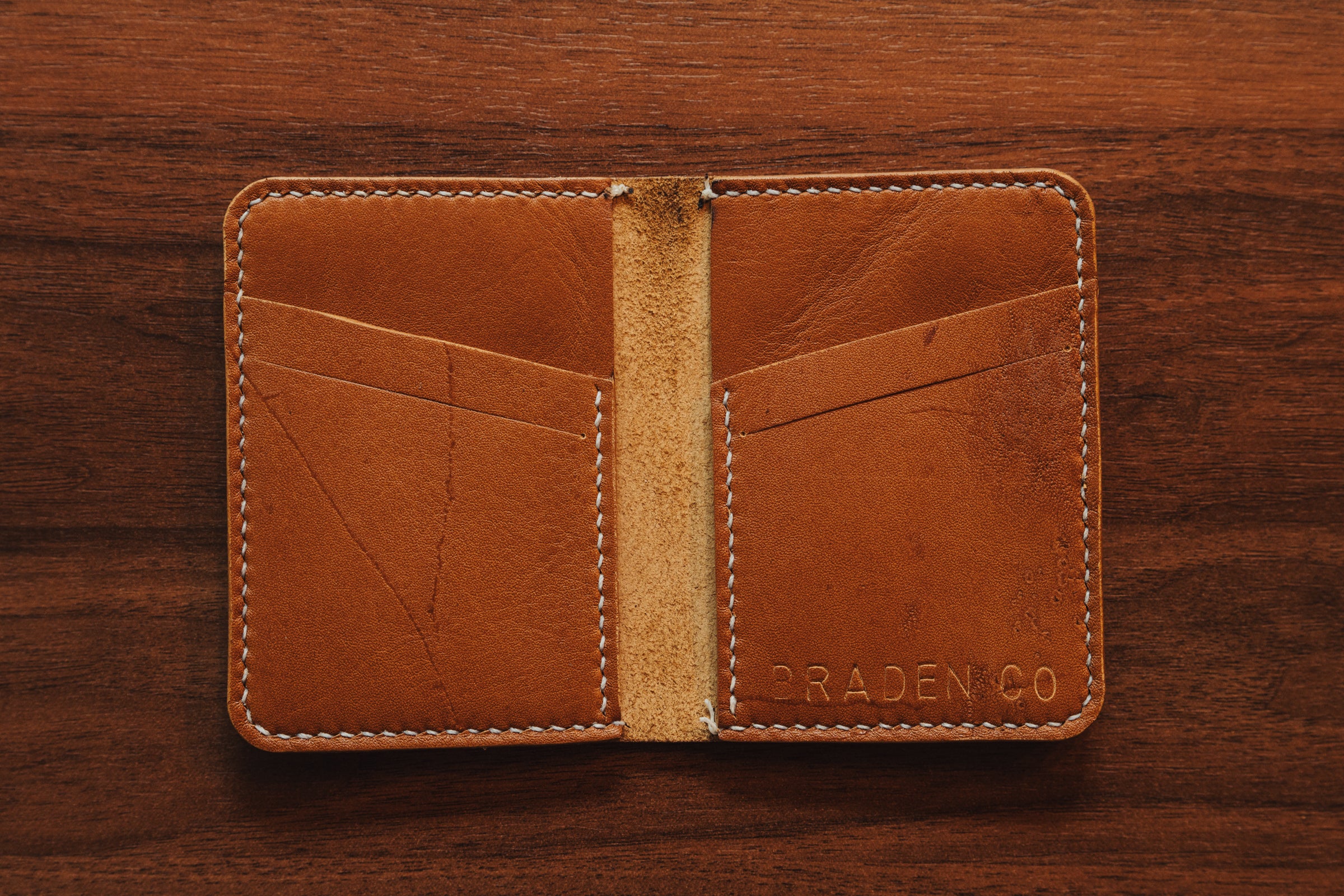Brown leather wallet with 'Braden Co' branding on a wooden surface