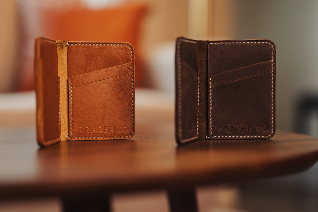 Two brown leather wallets on a wooden surface with a blurred background