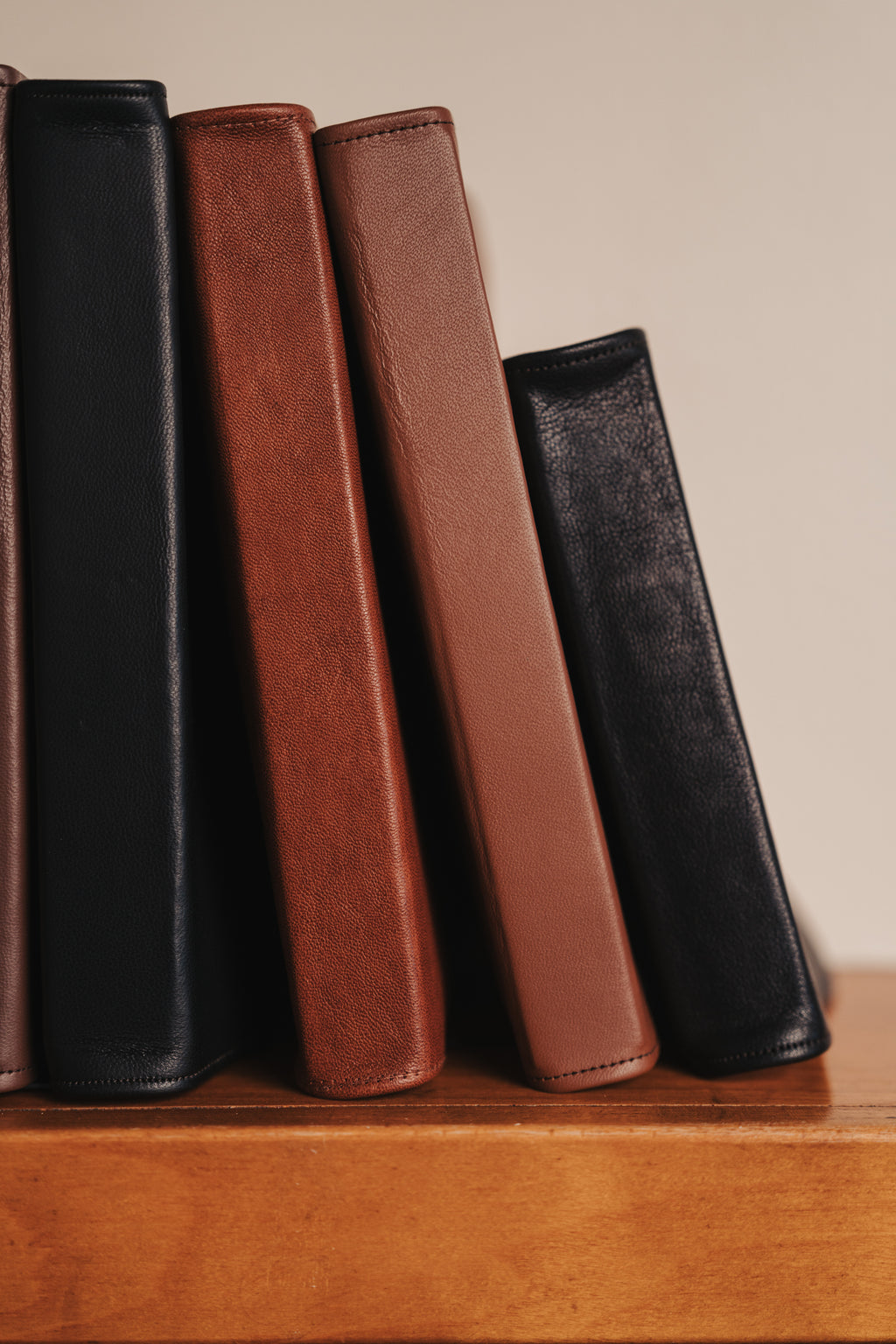 Four leather-bound books of different colors arranged on a wooden surface.