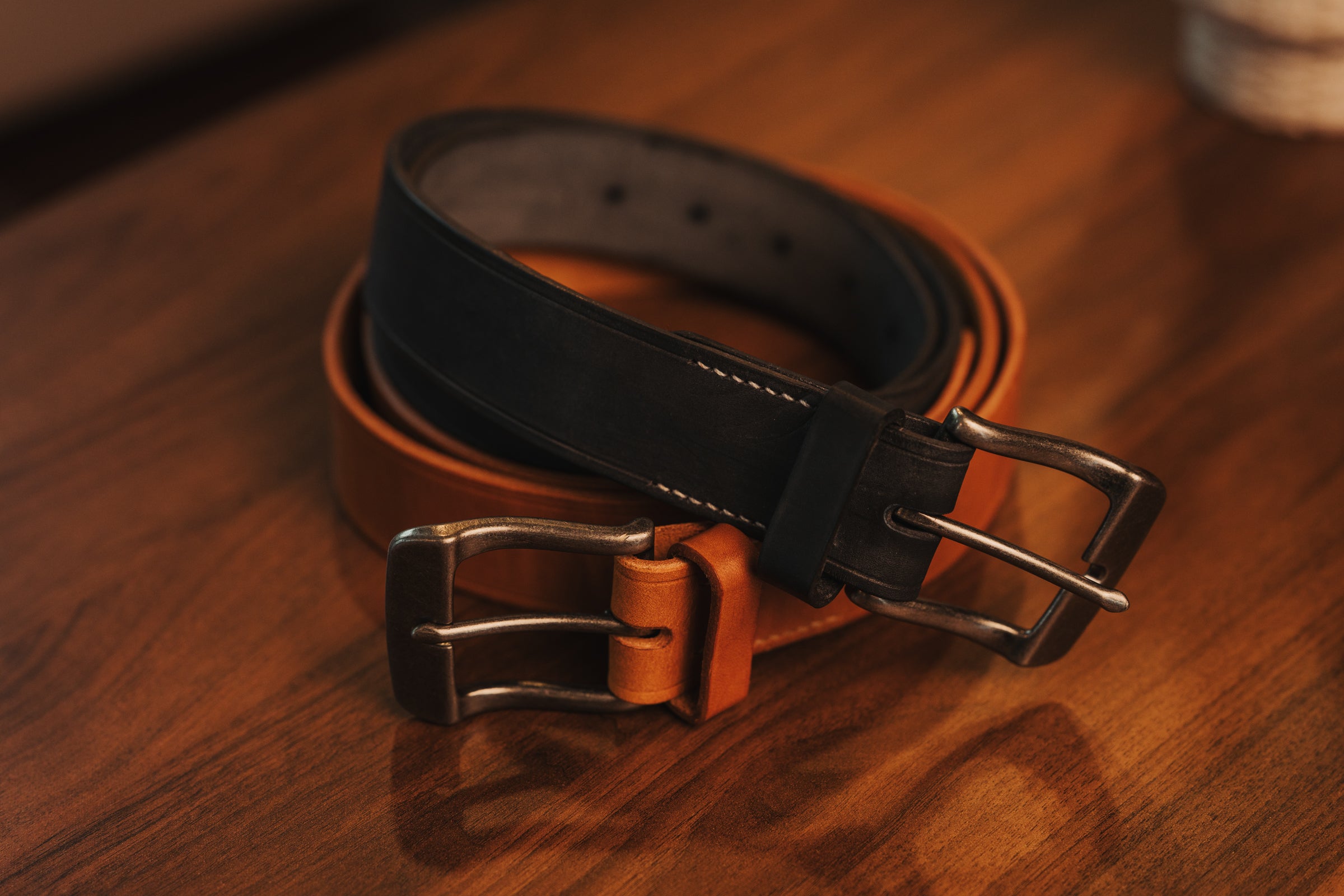Brown and black leather belt with metal buckles on a wooden surface
