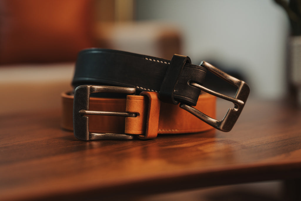 Two leather belts with metal buckles on a wooden surface.