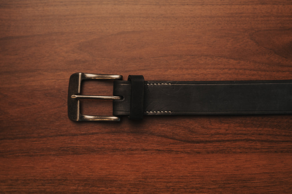 Black leather belt with a brass buckle on a wooden surface