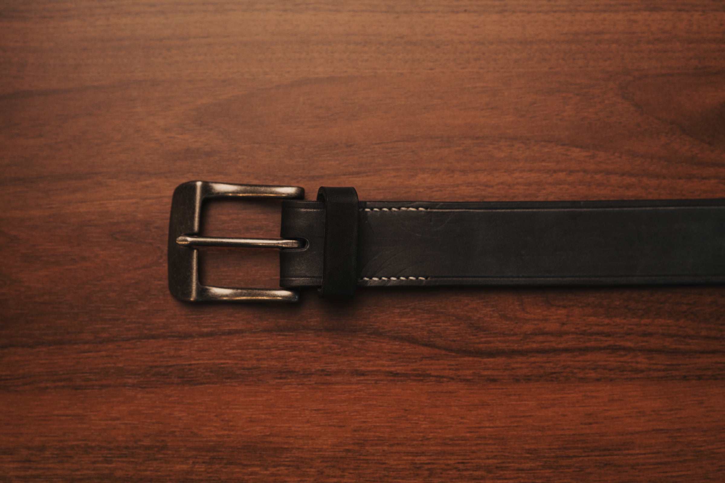 Black leather belt with a brass buckle on a wooden surface