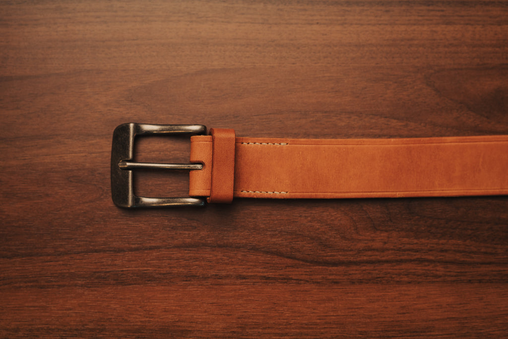 Brown leather belt with a metal buckle on a wooden surface