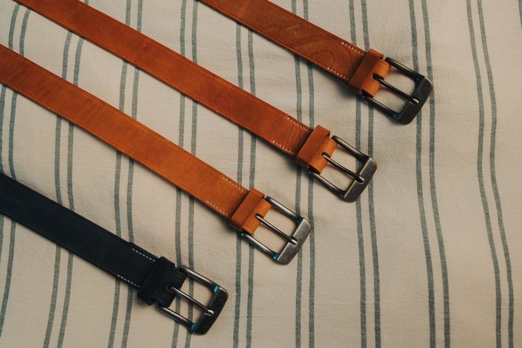 Four leather belts with metal buckles on a striped fabric background