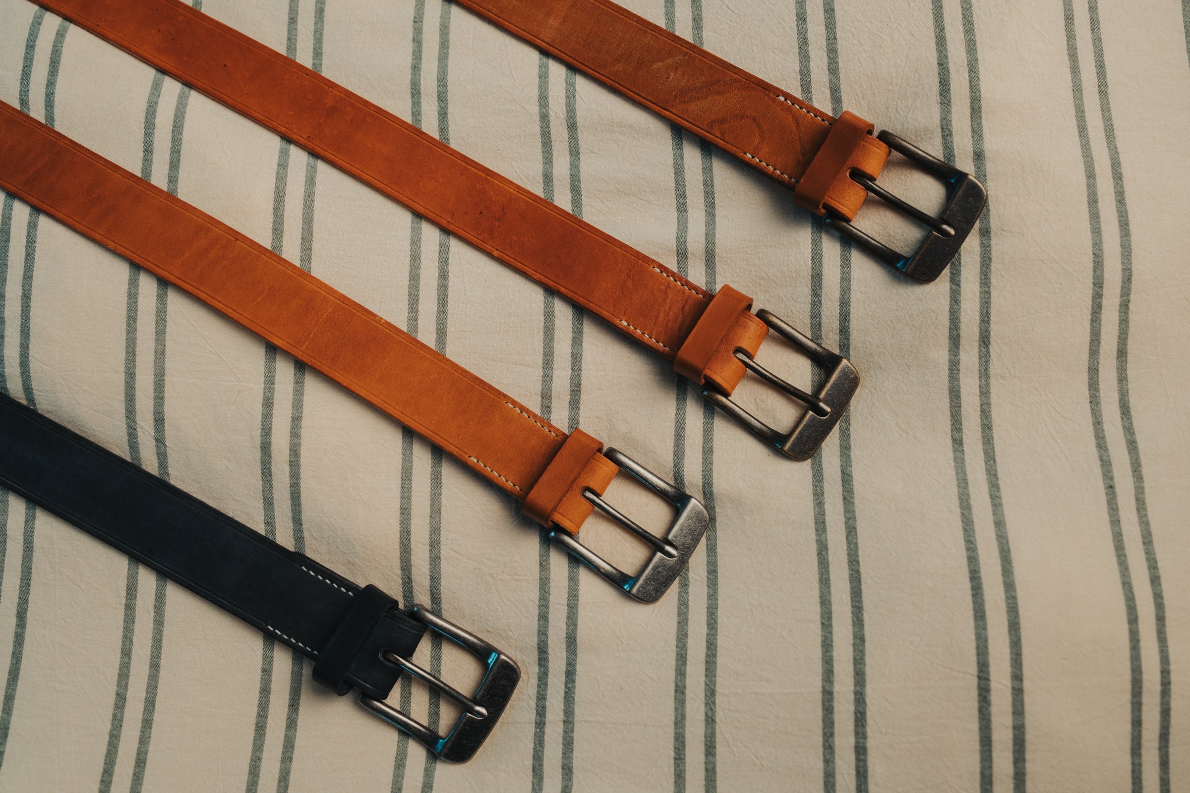 Four leather belts with metal buckles on a striped fabric background
